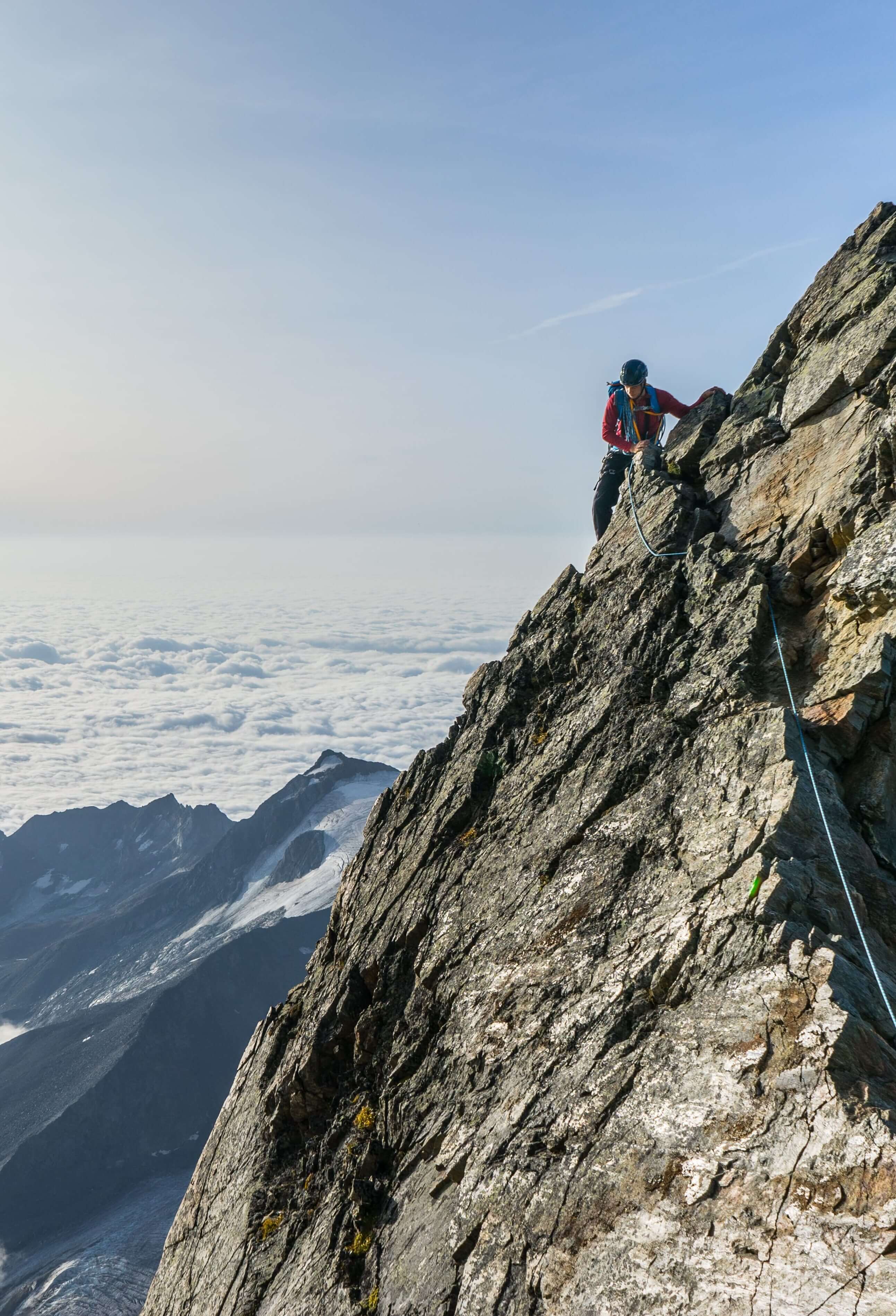 A person climbing a rock slope above the clouds