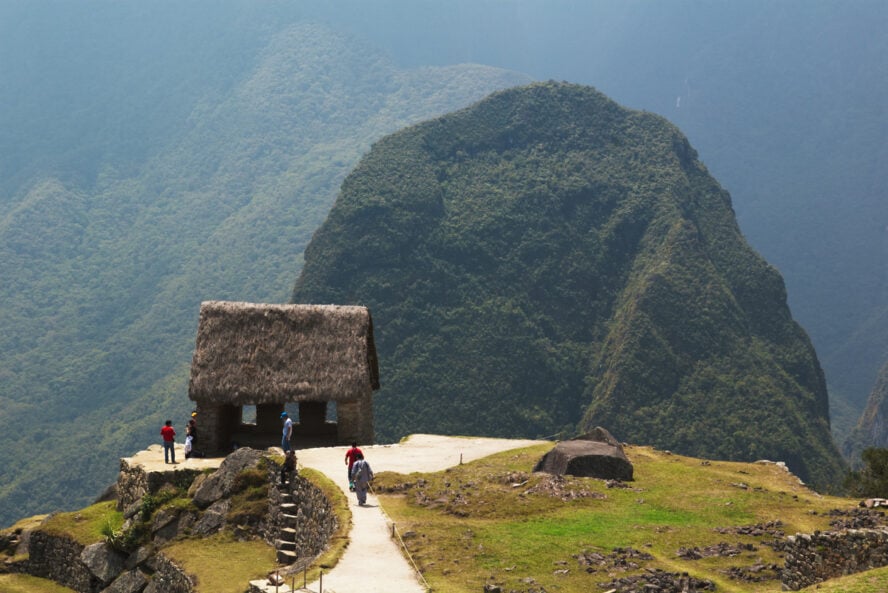 The stone Hut of the Caretaker with a thatched roof in the foreground, with the Funerary Rock in the background.