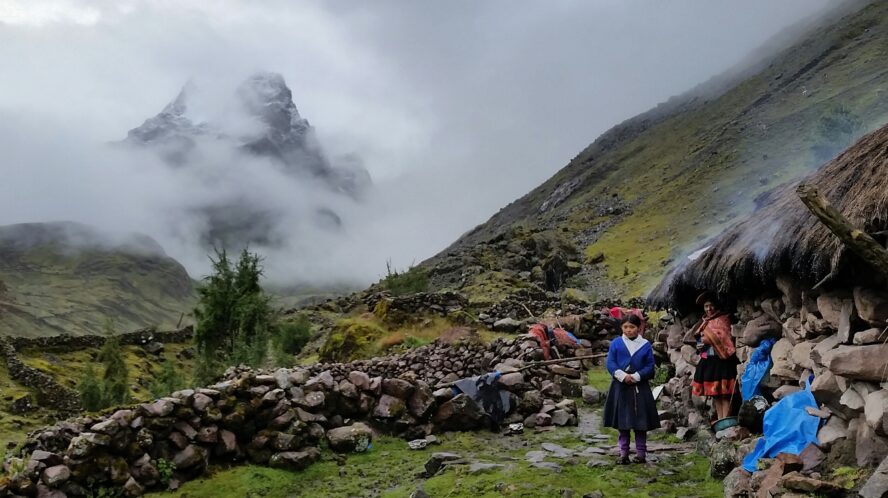 An Andean family in their village against a cloudy backdrop shrouding Pitusiray mountain.