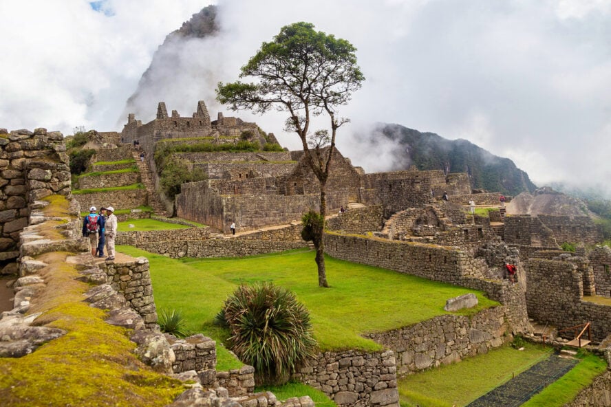 ravelers observing the ruins of Machu Picchu among wispy fog and green terraces.