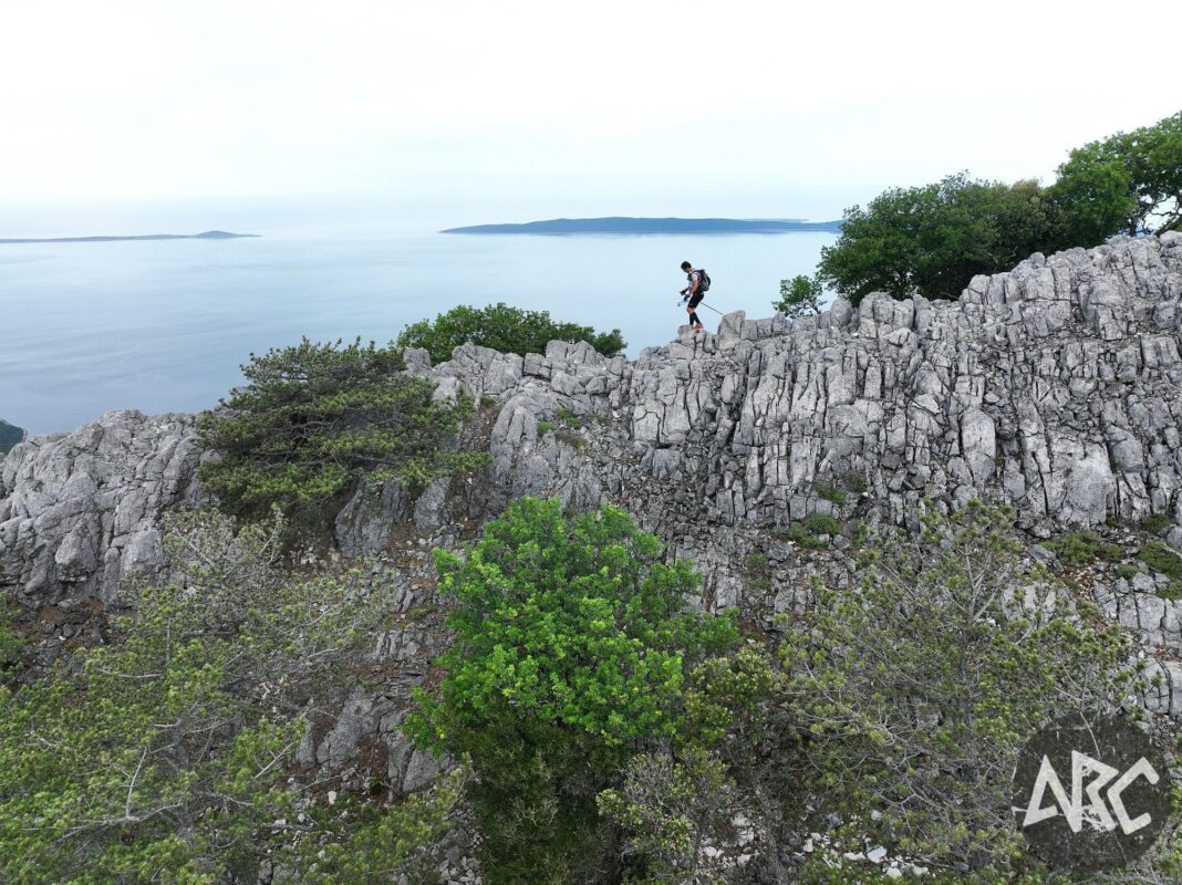 An adventurer scramling along a sharp ridge surrounded by the sea and trees