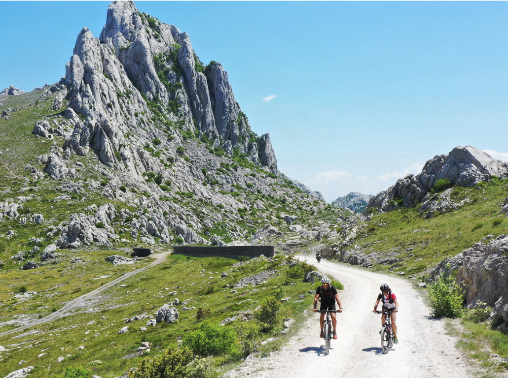 Cyclists riding down a macadam trail with spacious fields around them and Tulove Grede in the background