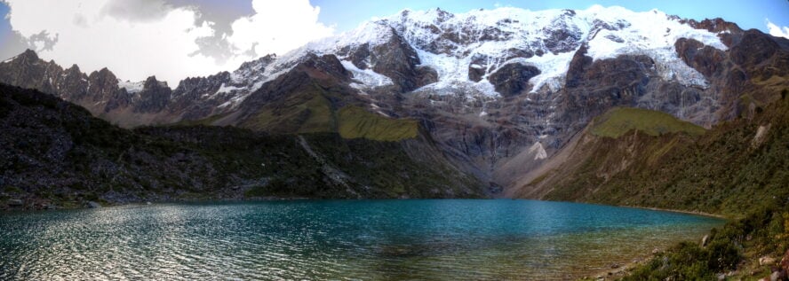  the blue Humantay Lake reflecting green grass slopes and a looming white capped mountain.