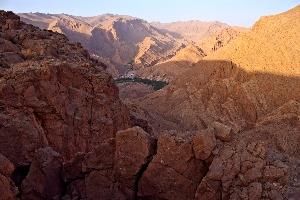 A view of a typical landscape in the area around Tinghir in Morocco with arid mountainous terrain with many canyons and small pockets of vegetation at the food of large cliffs.