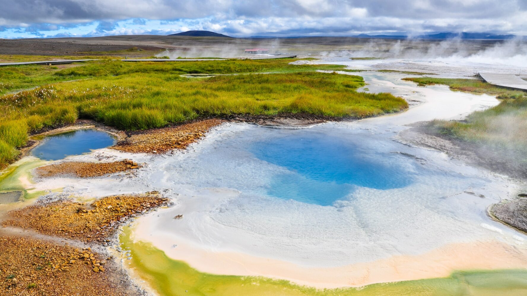 A crystal blue lake with steamy geysirs in the background