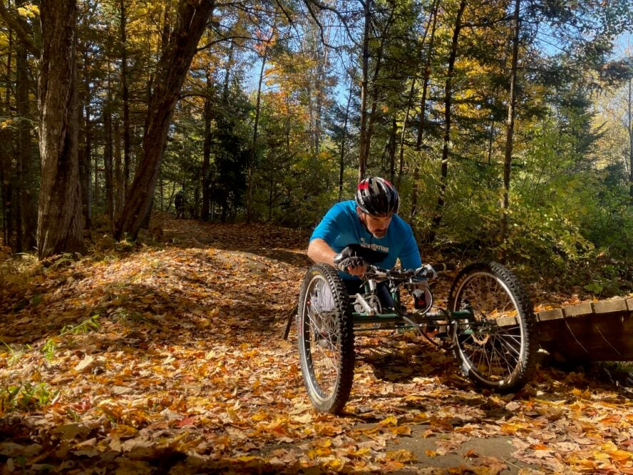 Handcyclist maneuvering over a leafy trail in the fall.