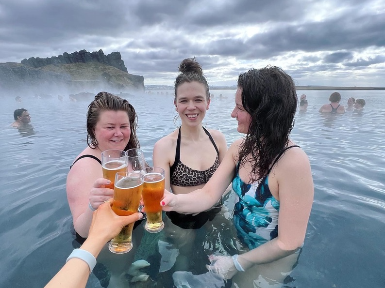 Group of friends relaxing in a hot spring and enjoying a cold beer.