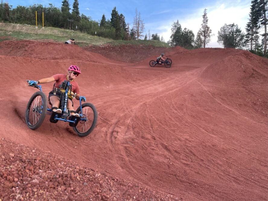 A group of handcyclists ripping down a wide red stone trail meant for any rider.