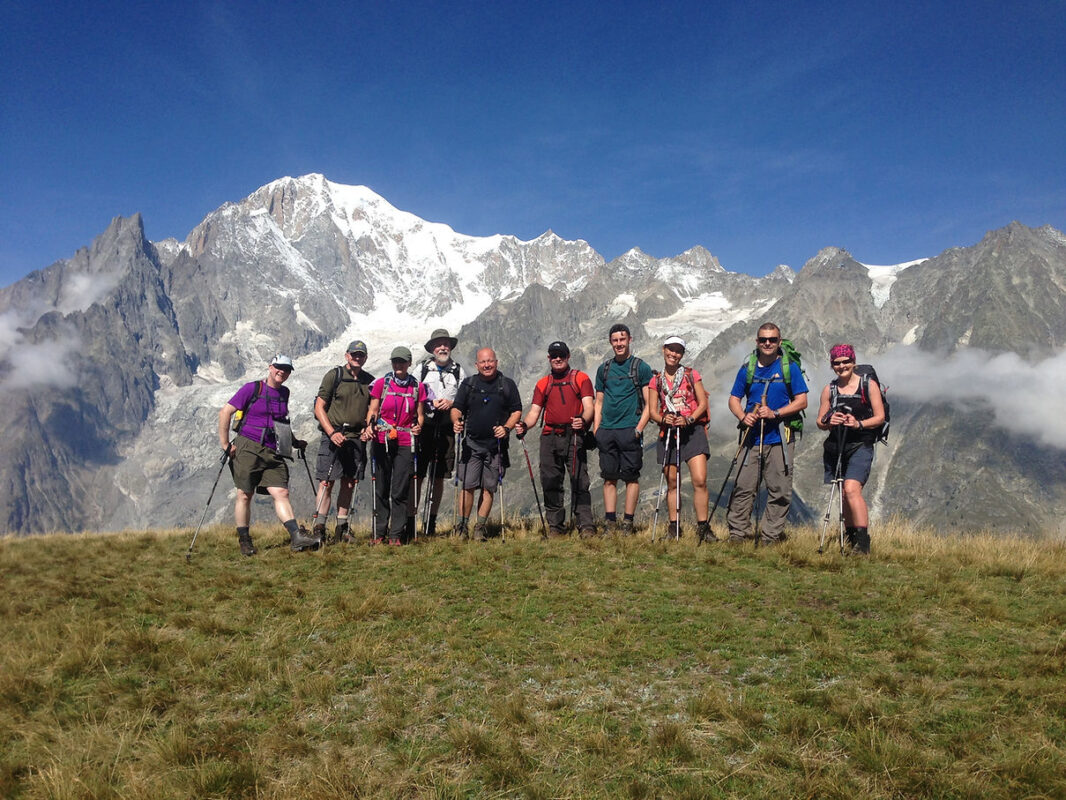 A group of hikers posing for a photo in front of rugged mountain peaks seen during their Tour du Mont Blanc trip.