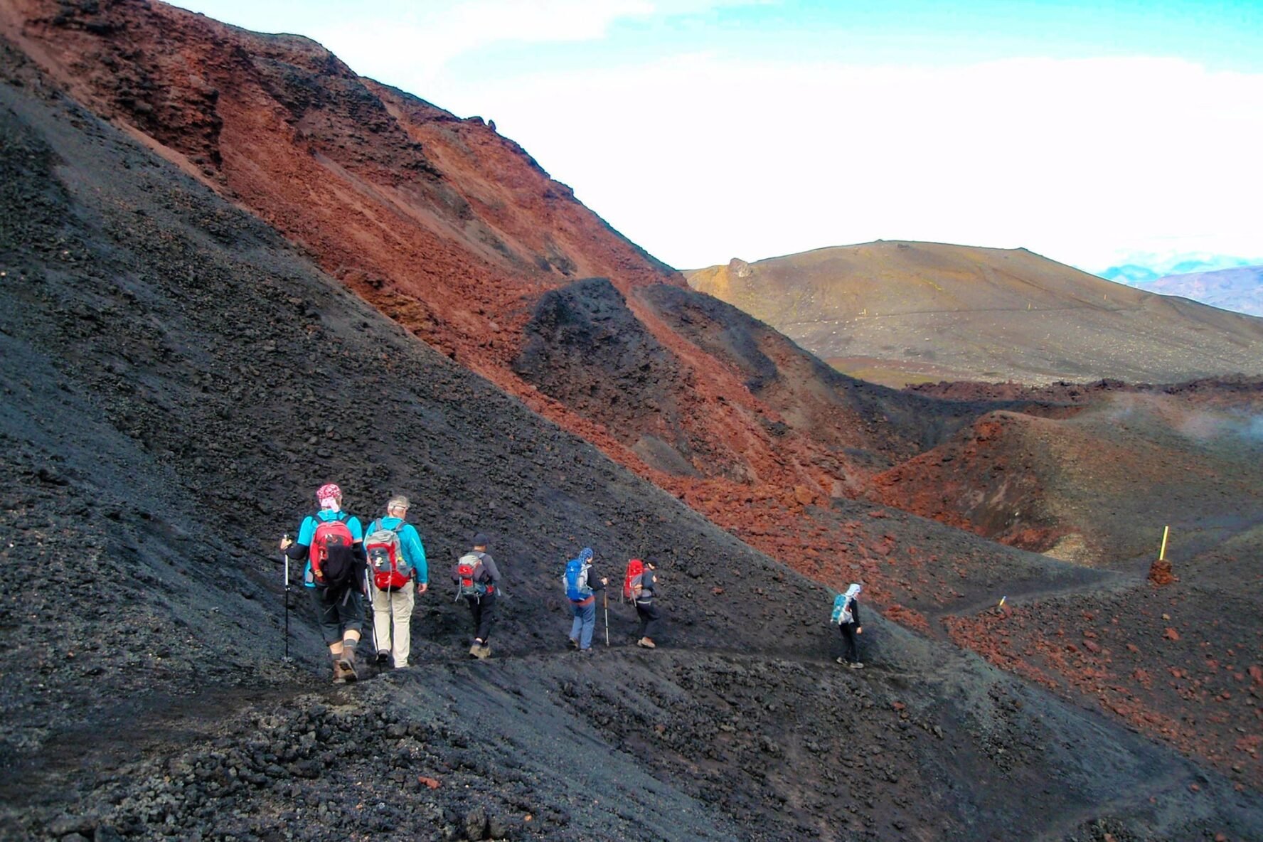 A group of hikers is walking surrounded by red-black volcanic terrain near Thorsmork, Iceland, photographed by Andrea Burgherr.