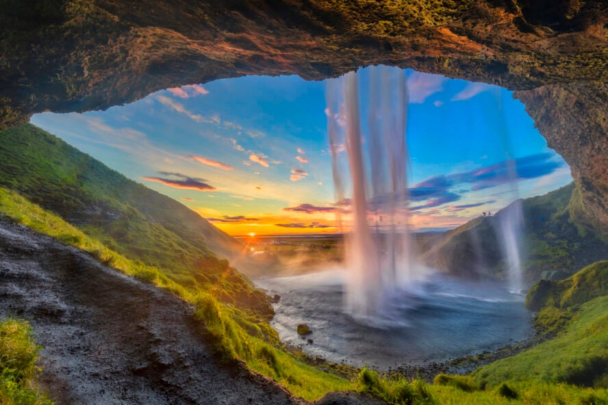 The narrow cascade of the Seljalandsfoss waterfall seen from a nearby cave at sunset