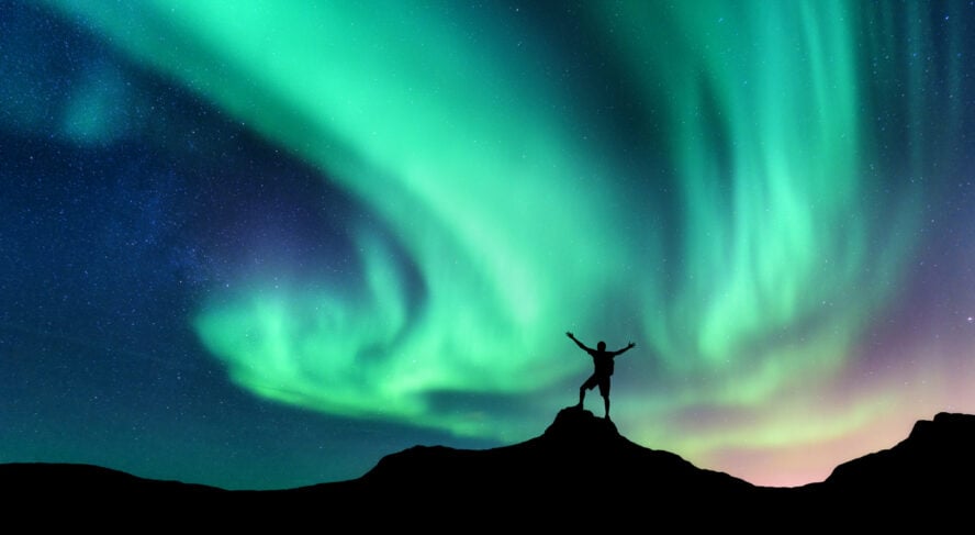 Hiker standing on a mountain at night under the northern lights