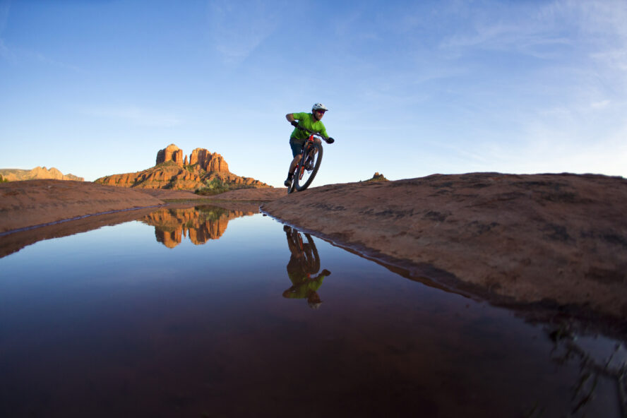 Mountain biker riding a slickrock trail with Cathedral Rock illuminated by sunset in the distance