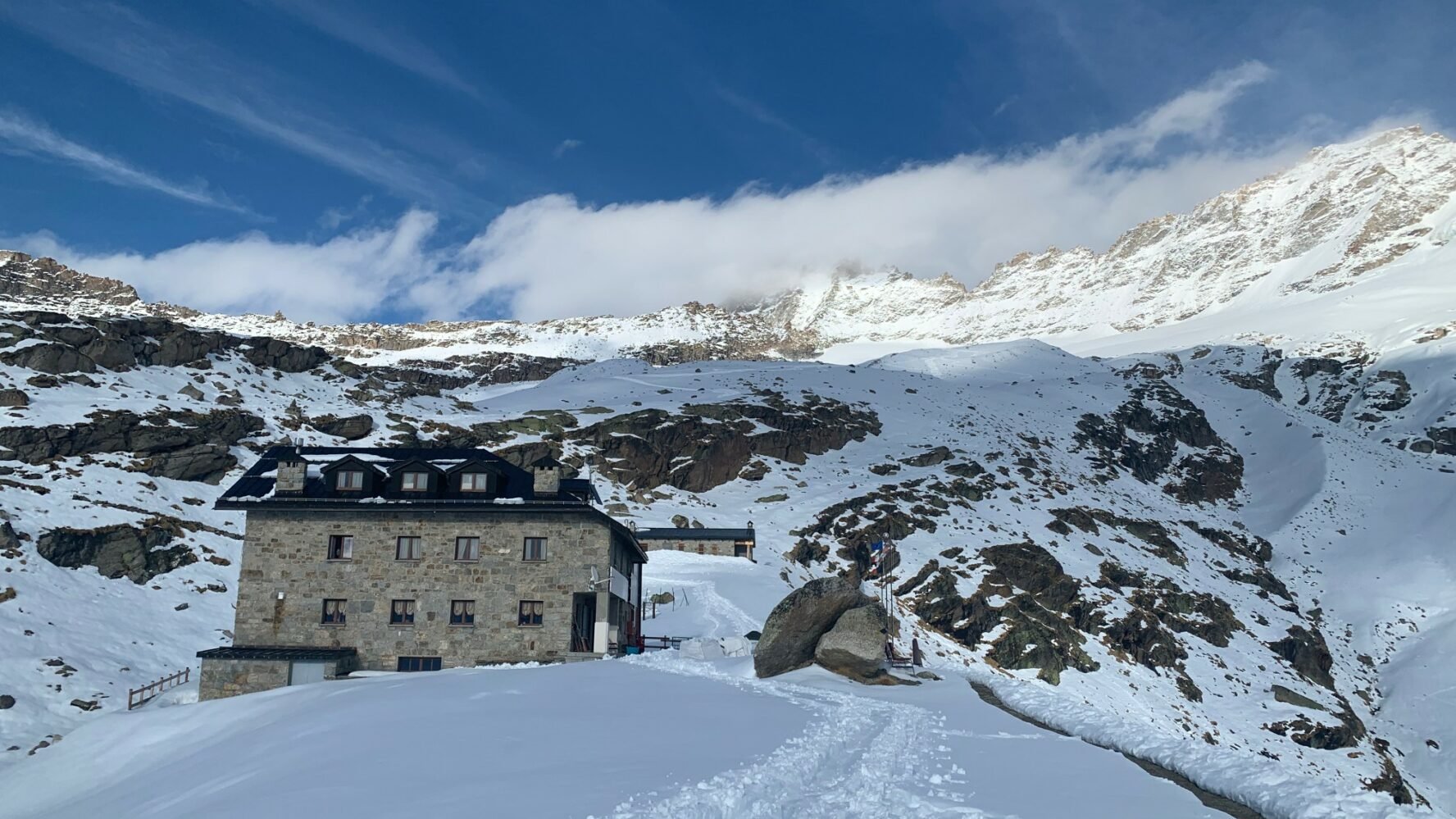 A stone mountain hut surrounded by Alpine landscapes used as accommodation during a summit ski touring trip of Gran Paradiso and Mont Blanc.