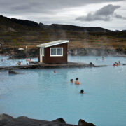 The nature baths sit in the foreground as people soak in the pools with beautiful views of the mountains rising in the background.