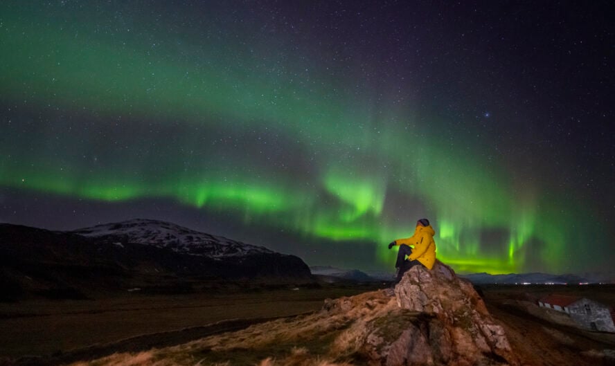 Person sitting on a rock observing the polar lights at night