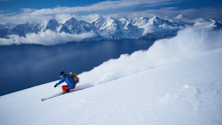 A skier shredding slopes in Norway’s Lyngen Fjord with the sea as a backdrop.