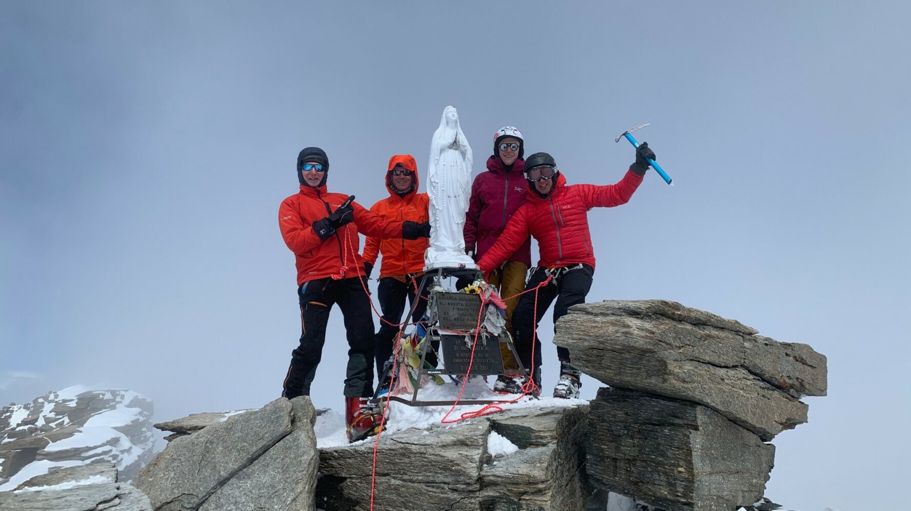 A group of backcountry enthusiasts on the top of Gran Paradiso posing for a picture with the sculpture of Madonna.