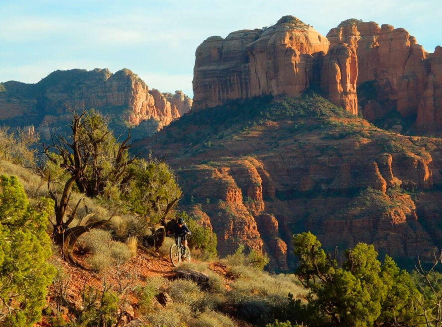 Mountain biker descending a rocky trail under the towering presence of Cathedral Rock