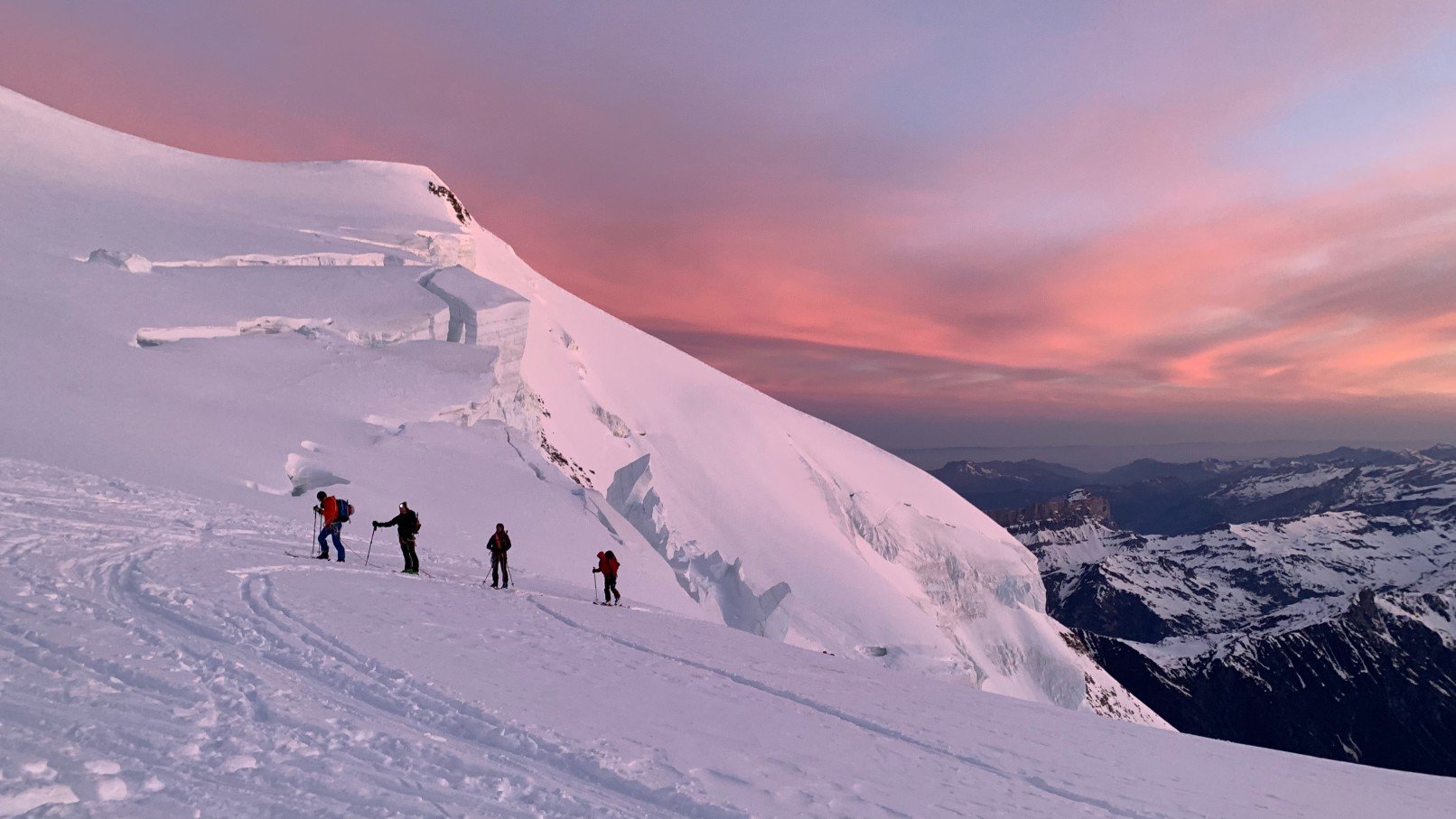 A group of backcountry skiers skinning a gradual slope near Mont Blanc during sunset.