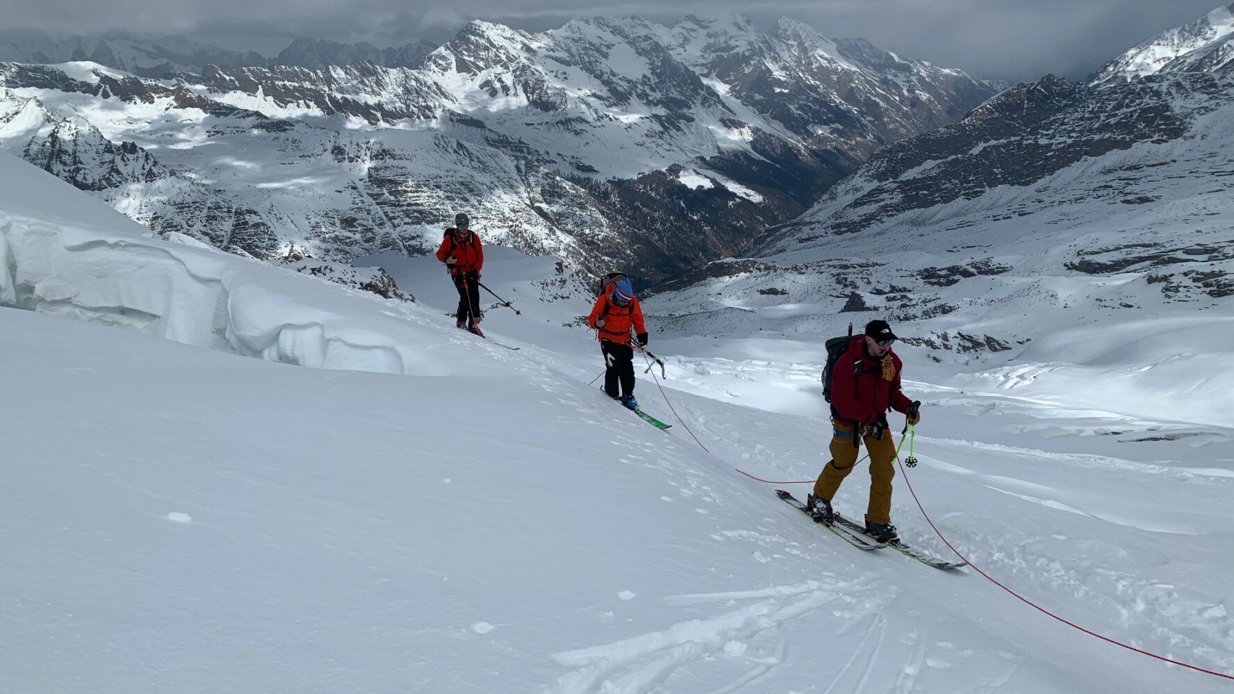 Three backcountry skiers traversing a snow-covered Alpine Valley with rugged peaks in the distance.