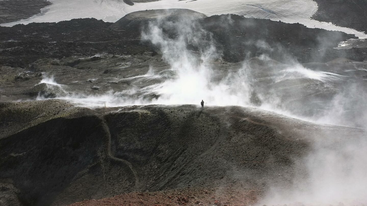 A hiker standing amidst s volcanic field shrouded in steam, photogrsphed by Jean-Christophe Bechet.