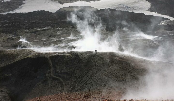 A hiker standing amidst s volcanic field shrouded in steam, photogrsphed by Jean-Christophe Bechet.