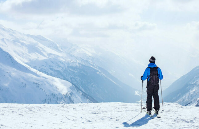 Skier overlooking a wintry valley with a snow covered mountain range in the distance.