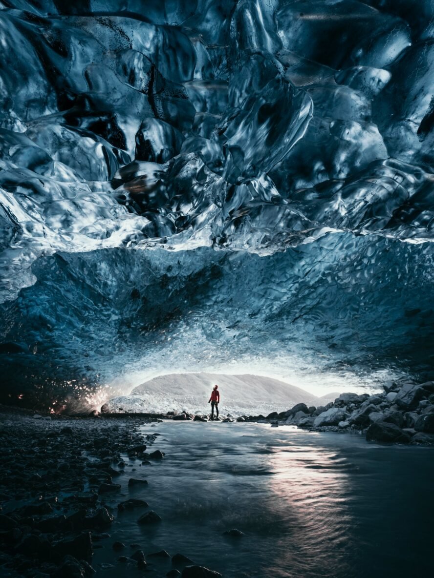 Hiker standing inside a glimmering blue ice cave in Iceland