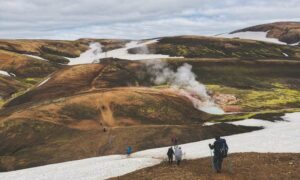 Hikers descend the trail with steaming hot springs in the background.