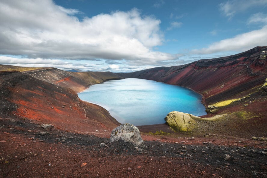 Ljótipollur, a crater lake, shines with bright blue water surrounded by red hues from the rocky flanks.