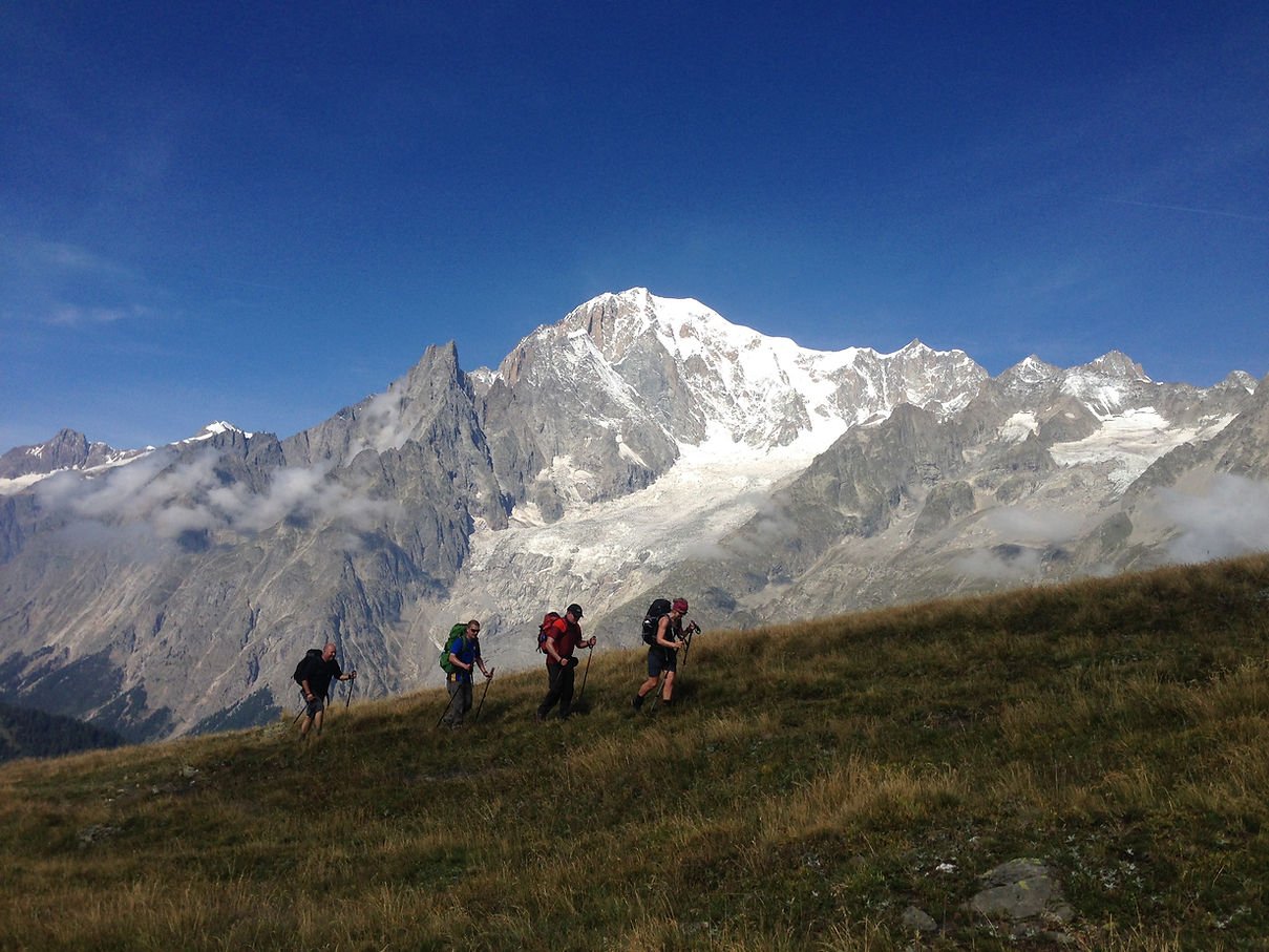A group of hikers ascending a hill during their Tour du Mont Blanc trek with a backdrop of rugged Alpine peaks.