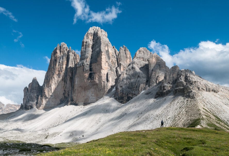 Lone hiker standing under the gigantic peaks of Tre Cime di Lavaredo in the Dolomites