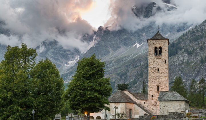 The Italian town of Macugnaga with a stone bell tower and a loft peak in the distance.