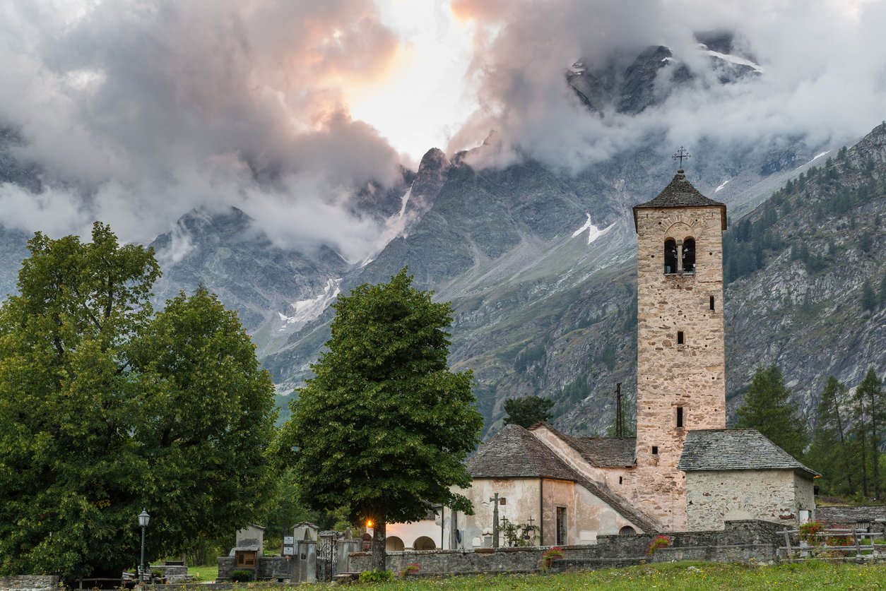The Italian town of Macugnaga with a stone bell tower and a loft peak in the distance.