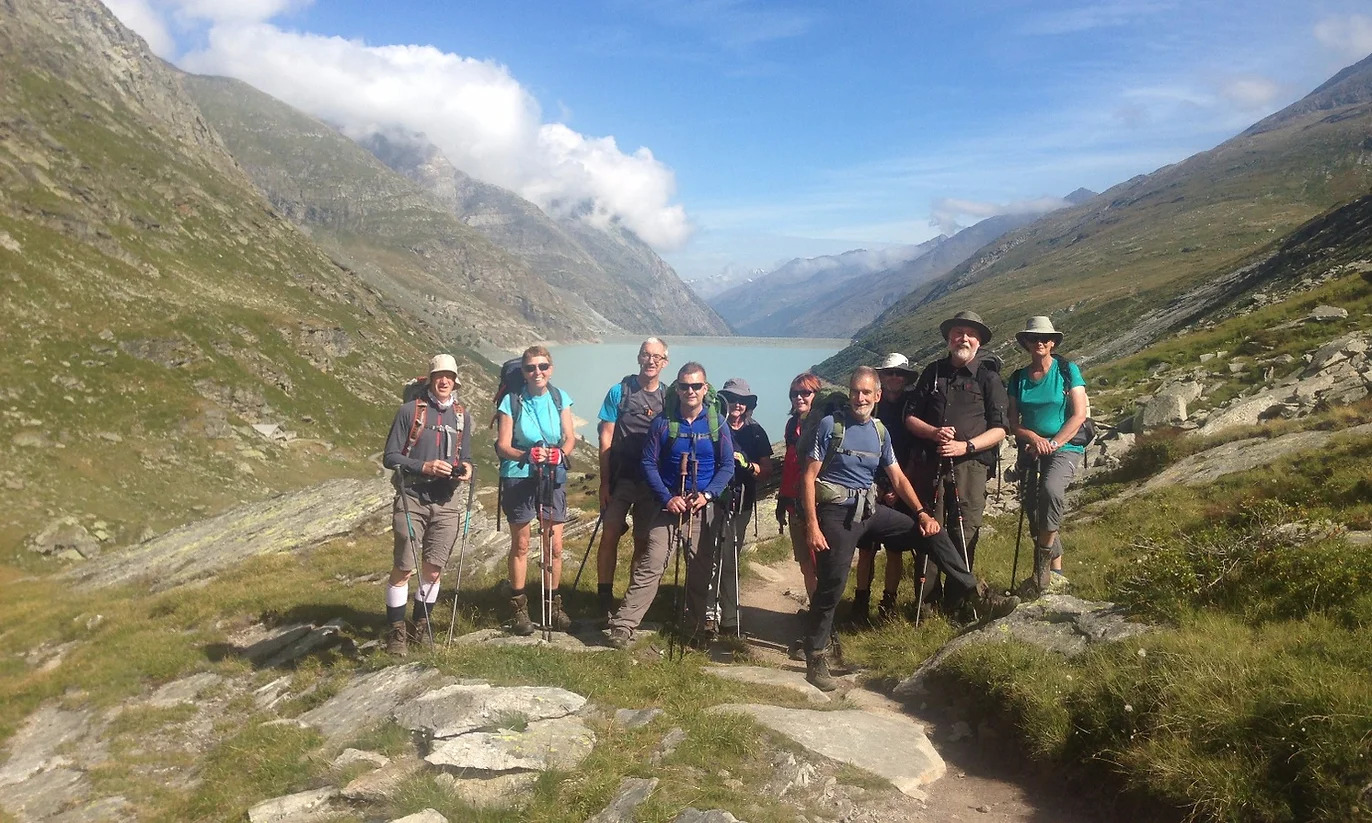 A group of hikers posing near the lake Mattmark, the beginning of their guided Tour de Monte Rosa hiking trip.