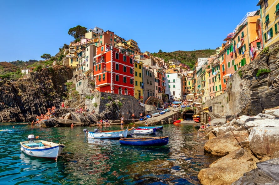 View of Riomaggiore on a bright sunny day, with tourists swimming in the cove.