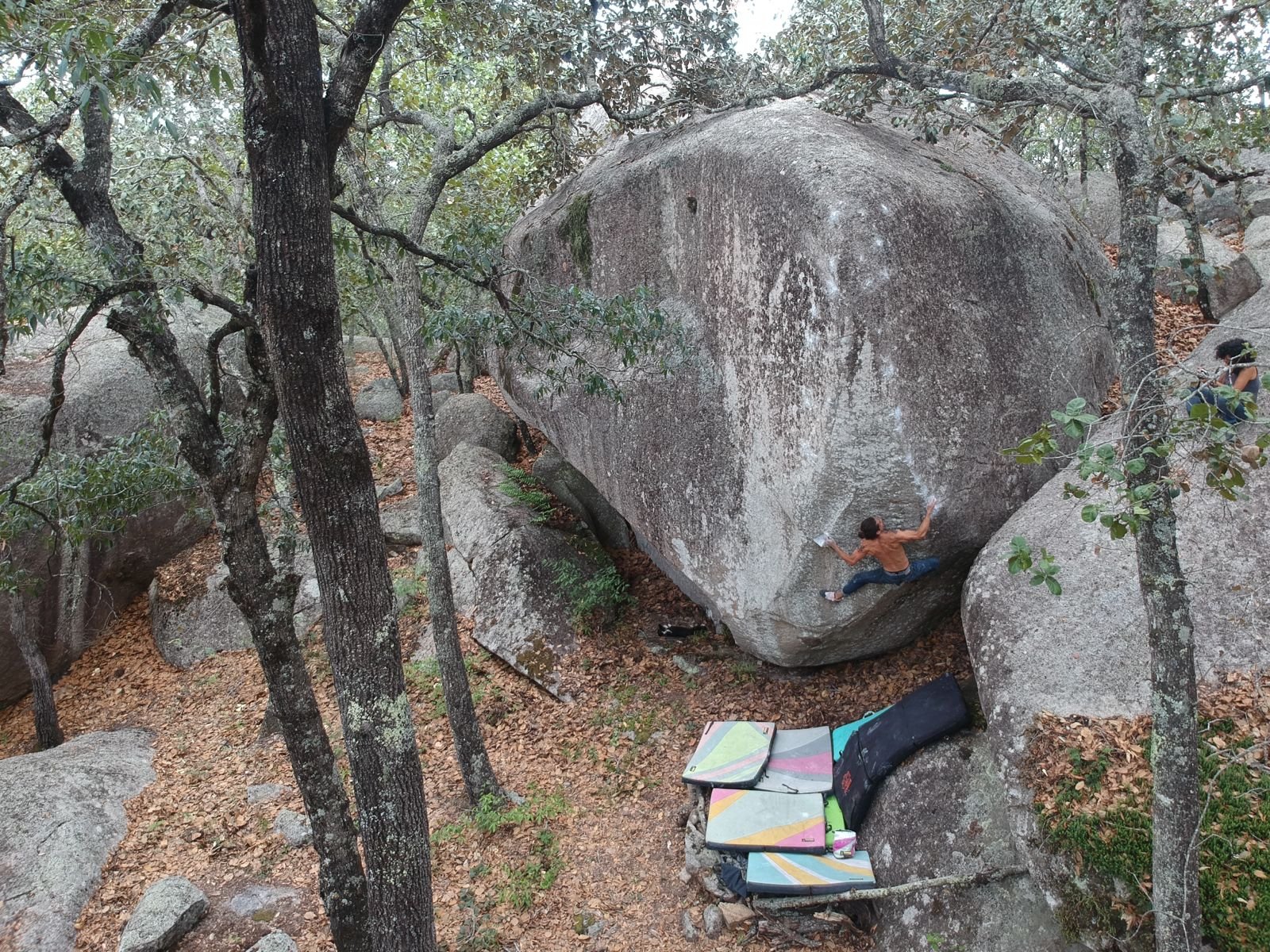 Rock climber bouldering on a crag with foam pads underneath them in Guadalcazar.