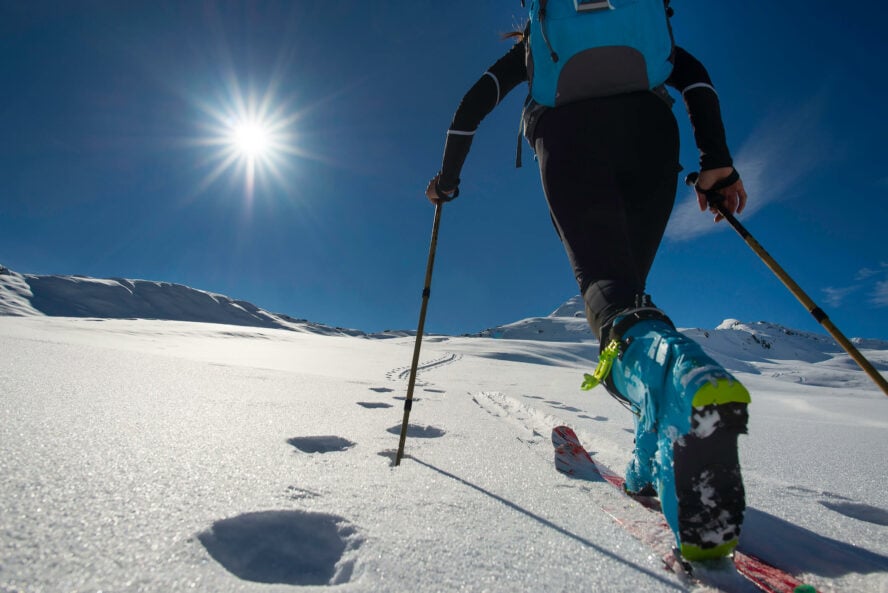 Close up of alpine touring bindings and skis, with a skier skinning uphill.