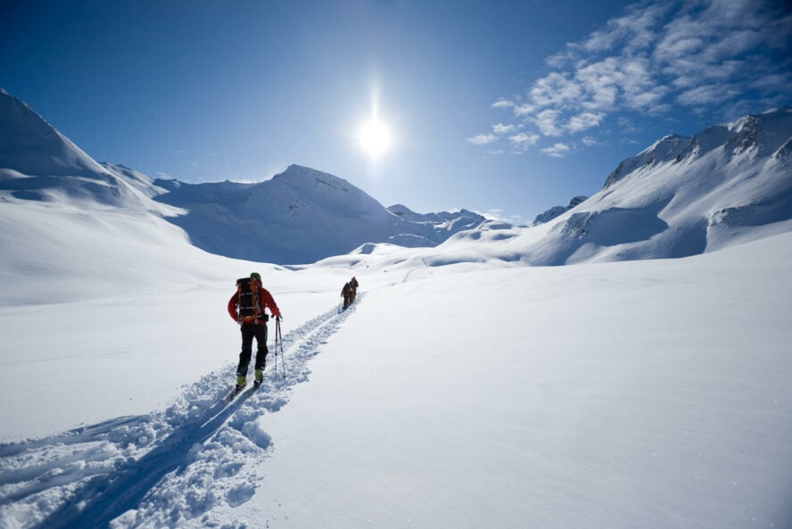 Line of ski tourers following a skin track with snow-covered mountains all around.