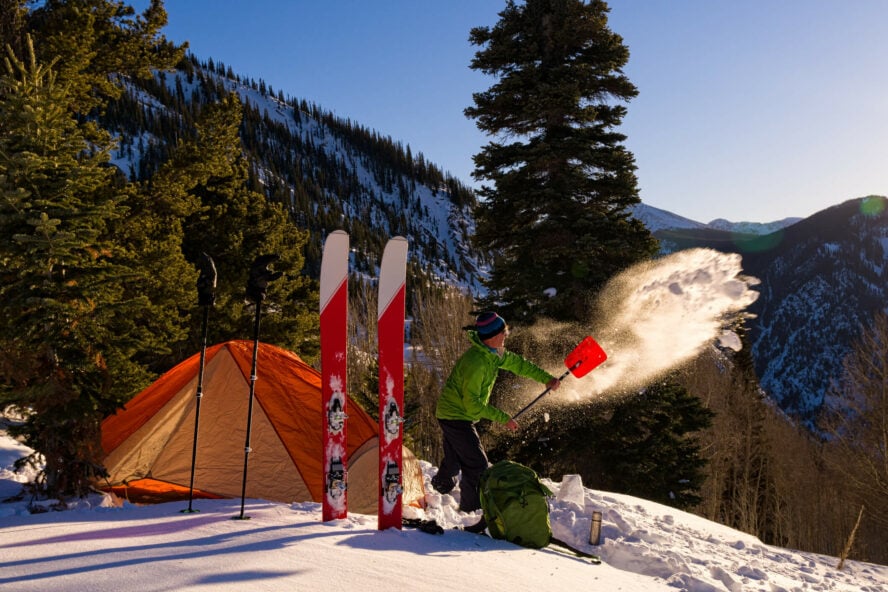 Man clearing snow for his camping spot after a day out ski touring.