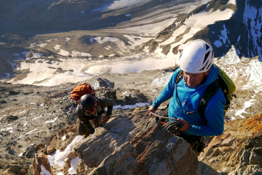 Two climbers approach the summit of Matterhorn, with expansive views of the valley below.