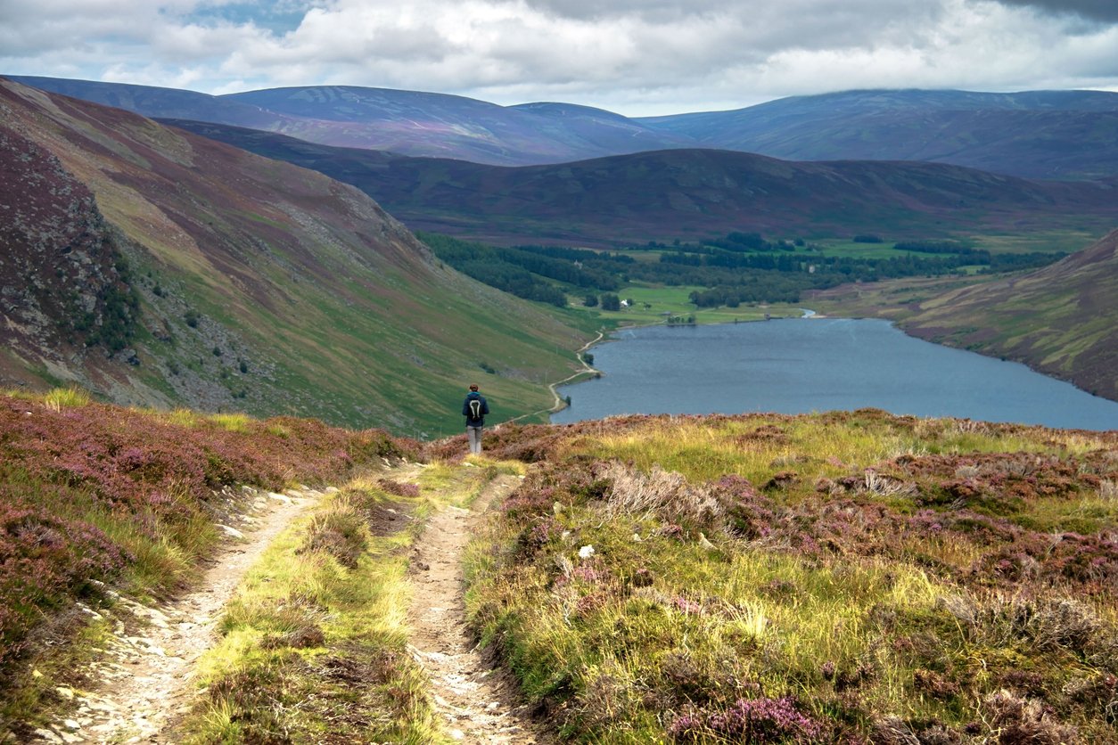 A hiker at a highpoint hiking along a path overlooking a lake in the Cairngorms NP, Scotland.