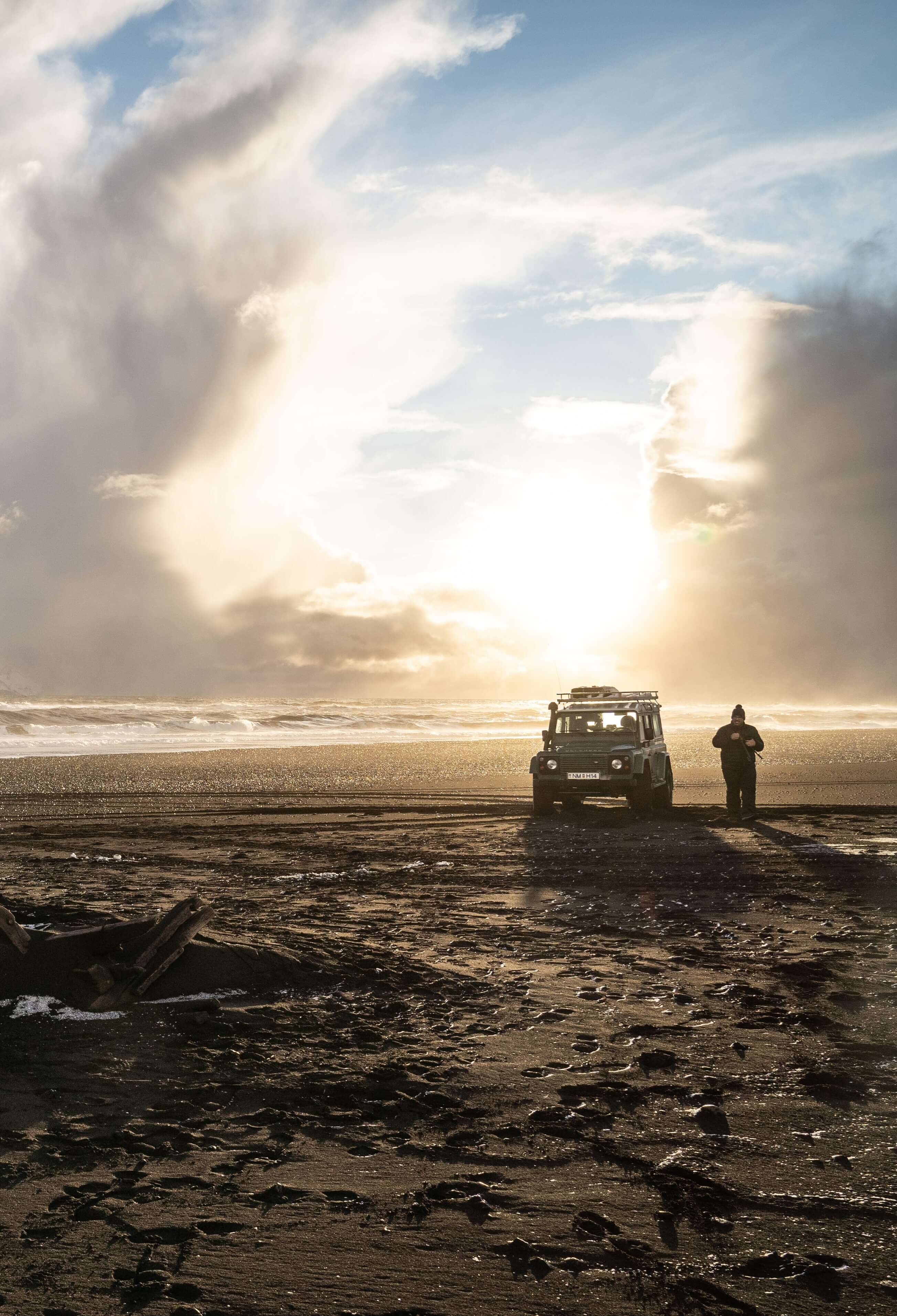 A person stading next to a jeep on a beach in Iceland during golden hour