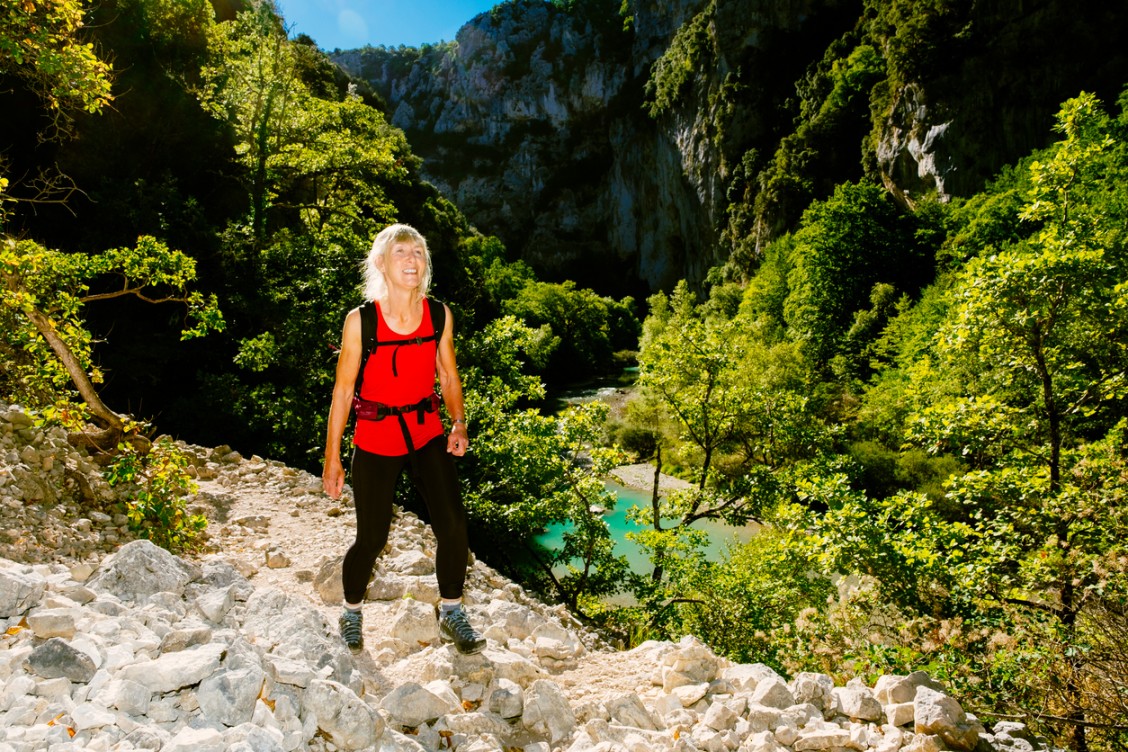 A hiker walking in the Verdon Gorge with visible cliffs and the turquoise river.