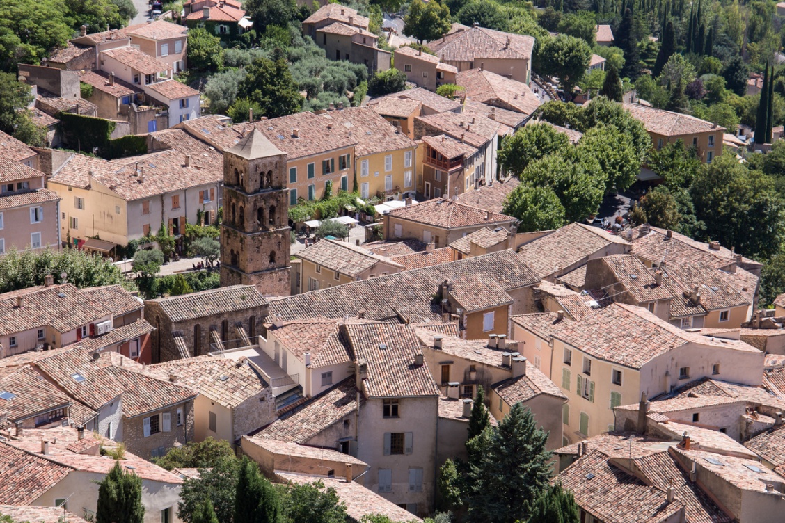 Aerial view of the medieval Provencal village of Moustiers-Sainte-Marie with stone houses with red rooftops and a bell tower.