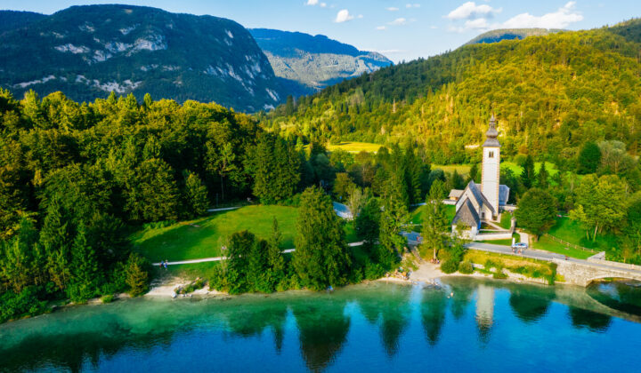 Lake Bohinj with a church that stands on its shore seen during hiking holidays in Slovenia’s Julian Alps.
