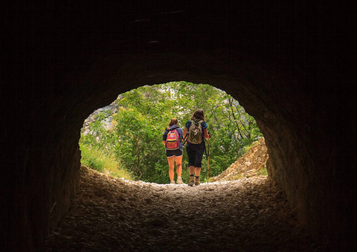 Two hikers hiking through a tunnel cut in the limestone in the Verdon Gorge.