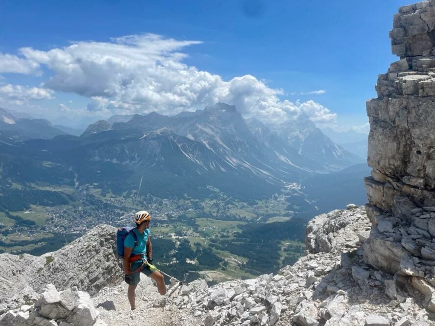 A rock climber standing at the foot of a Dolomite wall at the high elevation with views of Cortina d’Ampezzo and its valley and surrounding mountains.