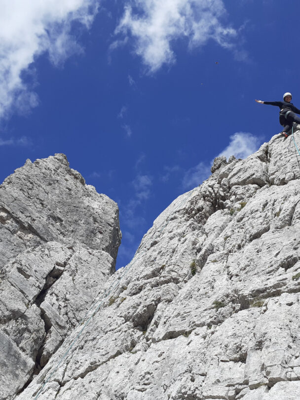 A rock climber standing at the foot of a Dolomite wall at the high elevation with views of Cortina d’Ampezzo and its valley and surrounding mountains.
